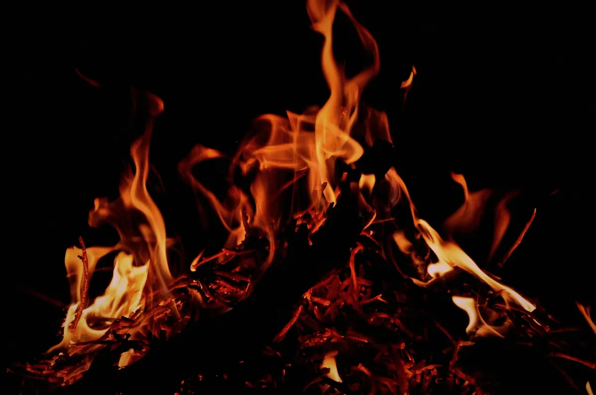 Oak logs burning on an open fire at night, flames rising from a bed of glowing embers