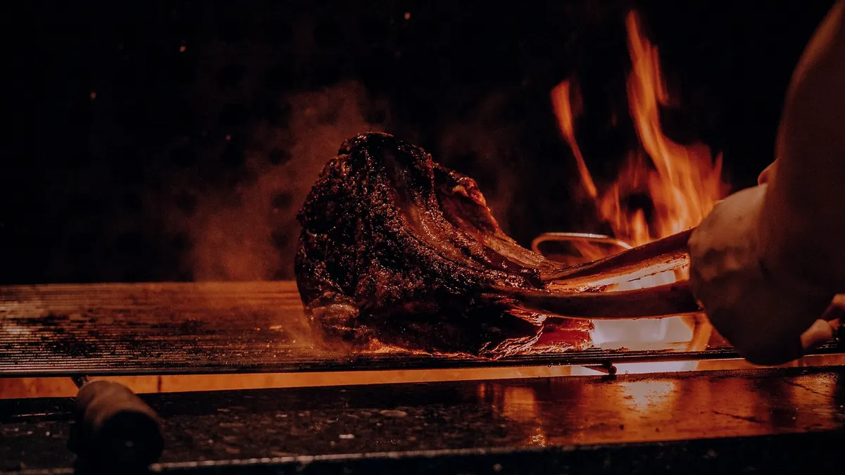 A cook holding a bone-in rib of beef over the fire
