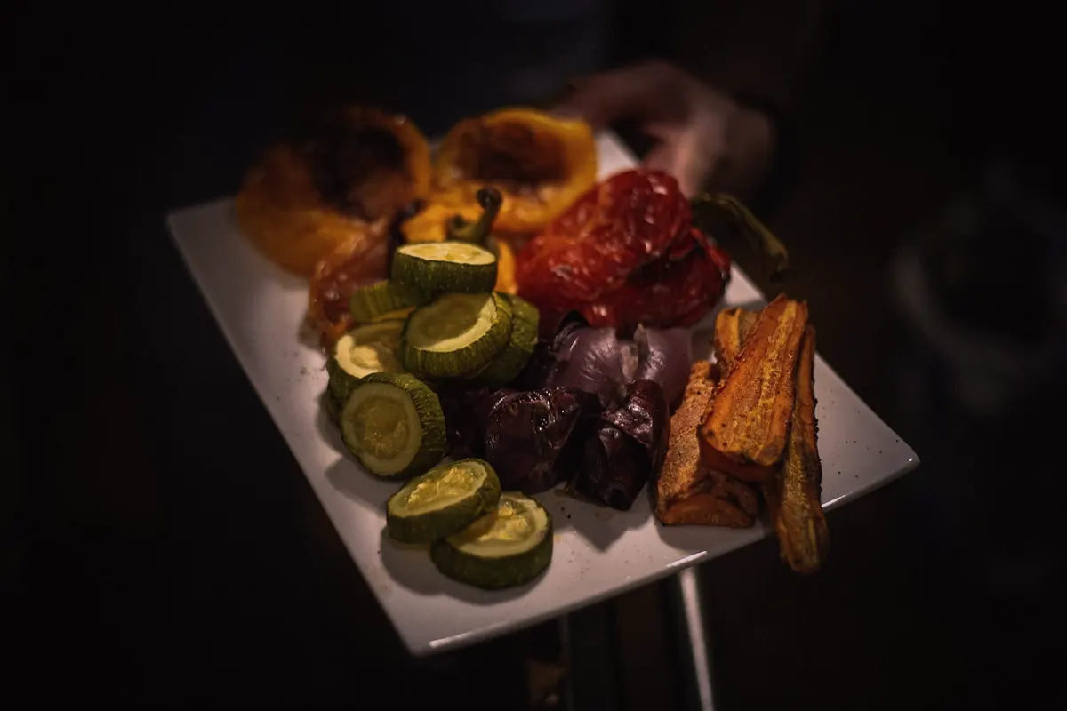 A plate of grilled vegetables held out in a dark room