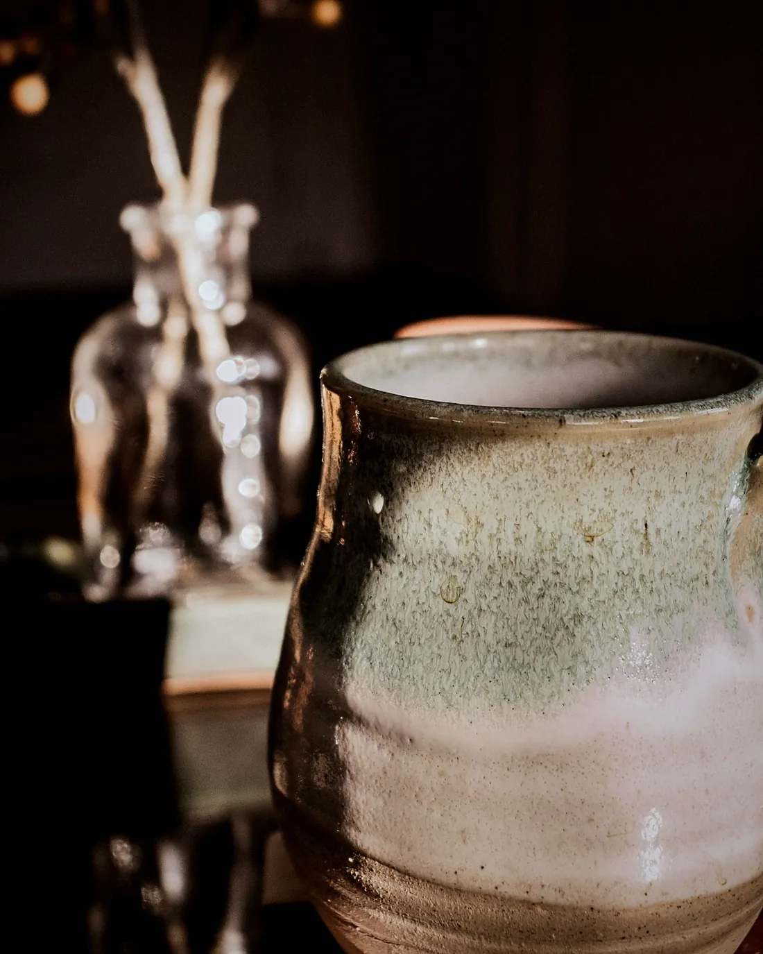 A tall jar with a handle in a pale green glaze, lit by a lamp