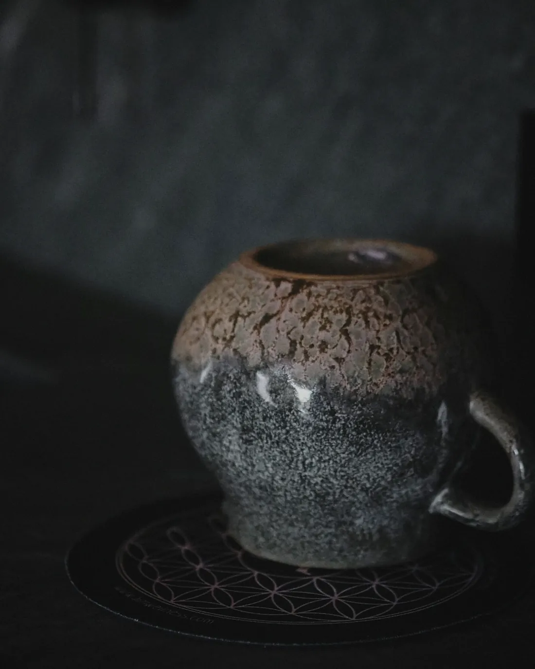 A grey speckled mug with a rust brown rim on a dark coaster