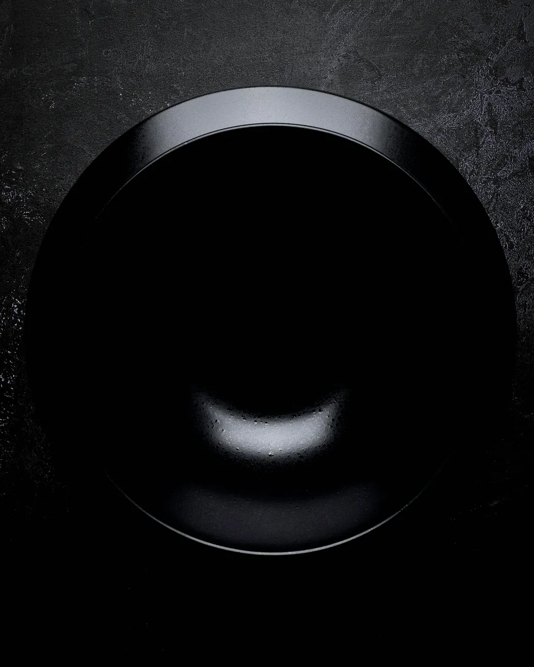 A black glazed plate seen from above on dark stone