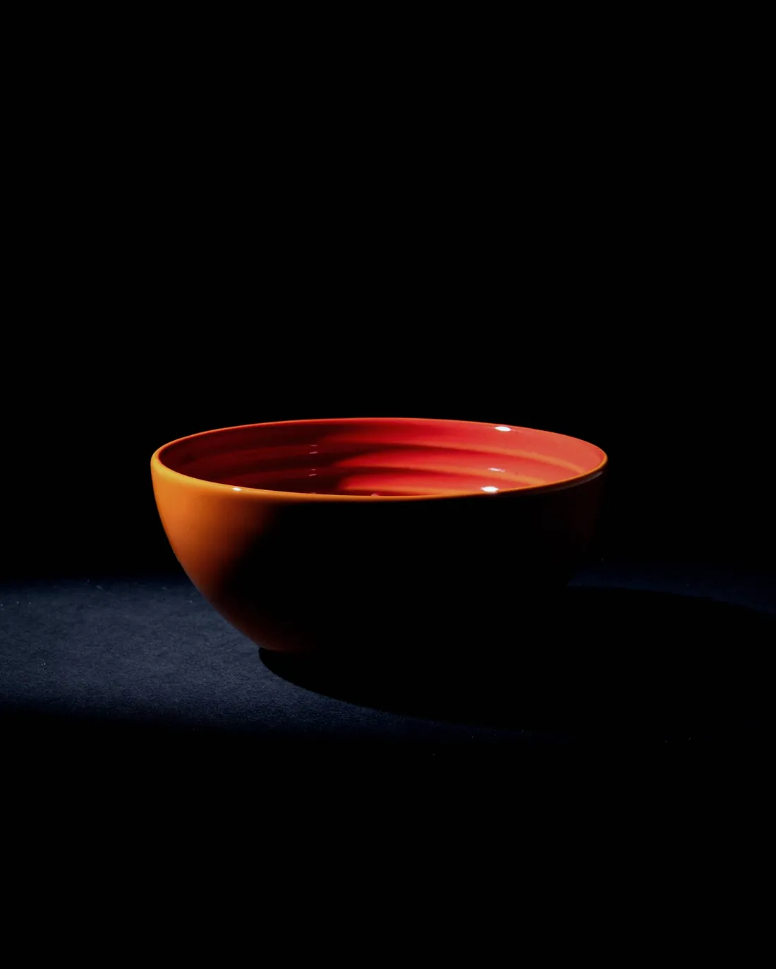 A small bowl glazed red inside, lit from the left on a dark cloth