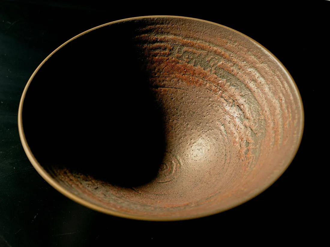 A wide serving bowl with an iron speckled glaze, lit from the right