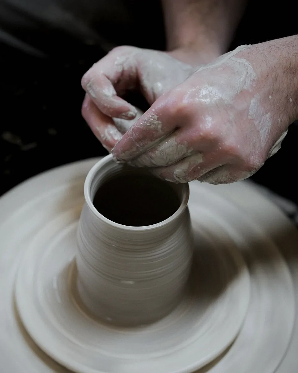 Wet hands lifting the wall of a white clay cylinder on the wheel