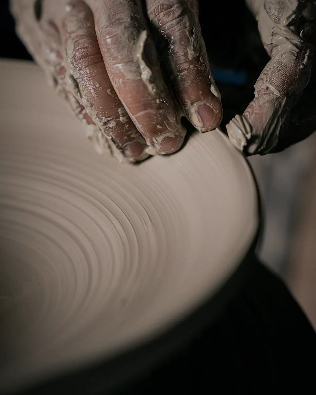 Two hands shaping a wide, flat plate on a turning wheel