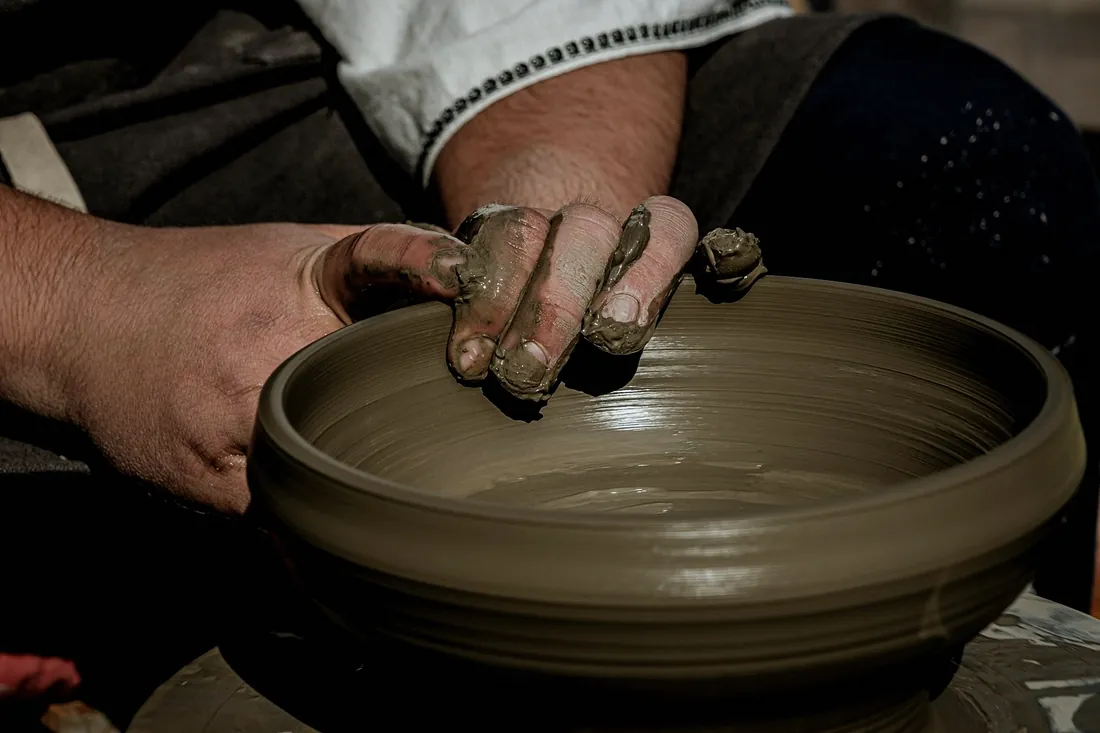 Hands resting on the rim of a wide grey bowl on the wheel