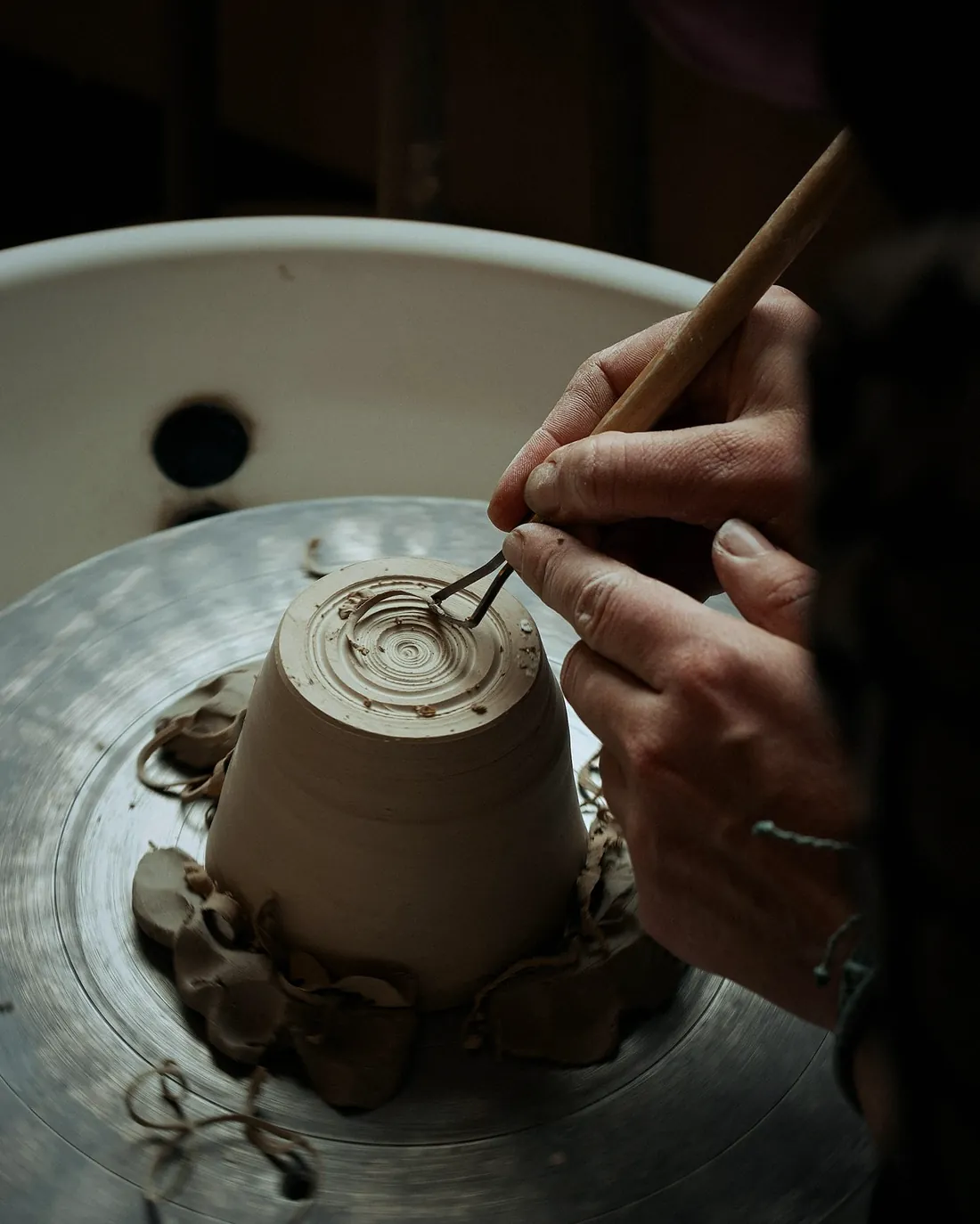 A wooden tool trimming the foot of an upturned cup on the wheel