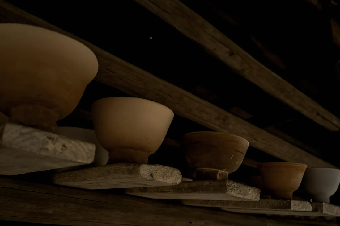 Rows of unfired bowls drying on wooden shelves in the studio