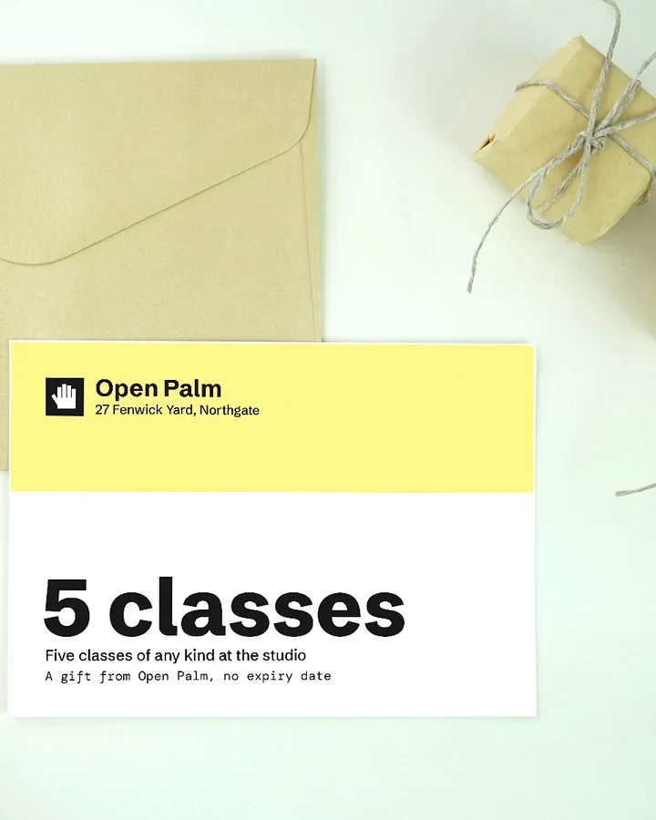 An Open Palm gift card for 5 classes beside yellow lilies and small wrapped parcels