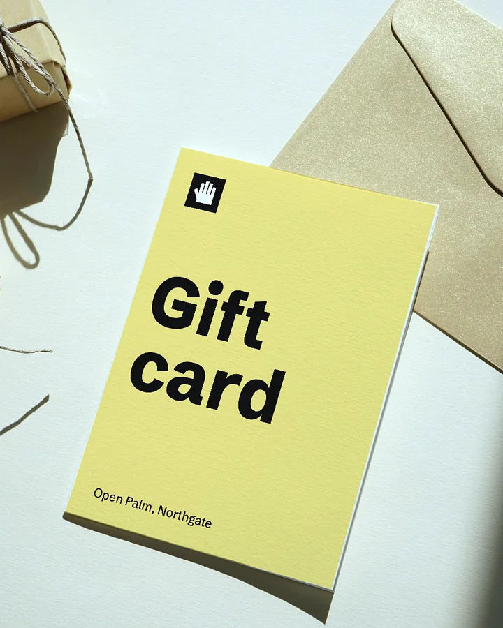 A tall yellow Open Palm gift card on textured paper next to an envelope and two wrapped parcels
