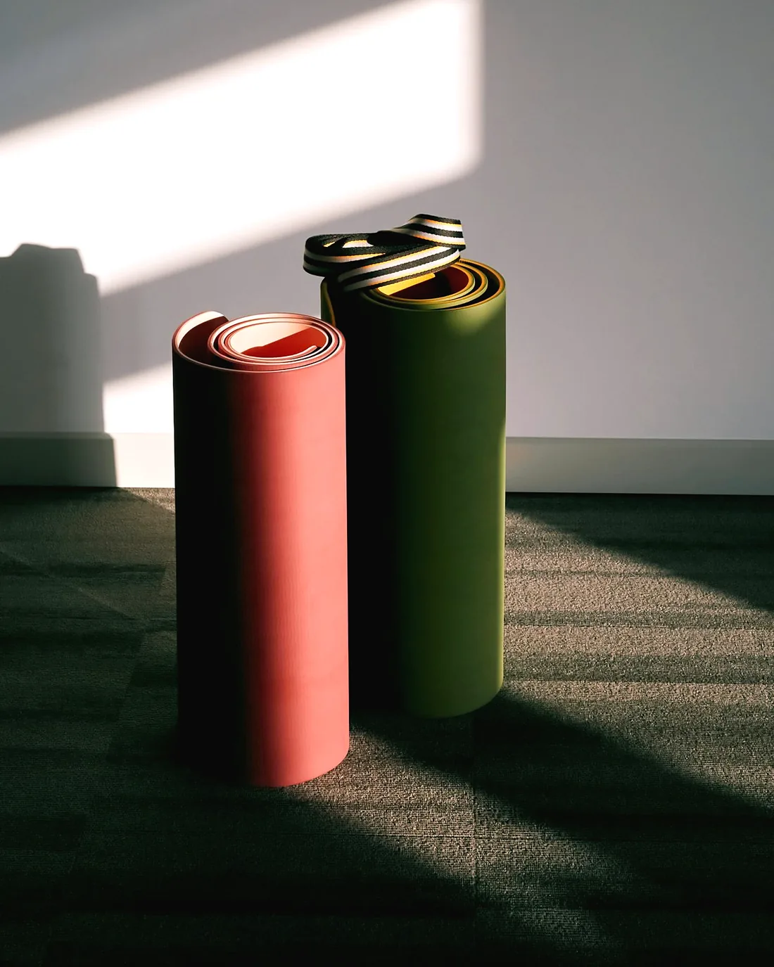 Two rolled rubber mats, one red and one forest green, standing on end in a sunny room