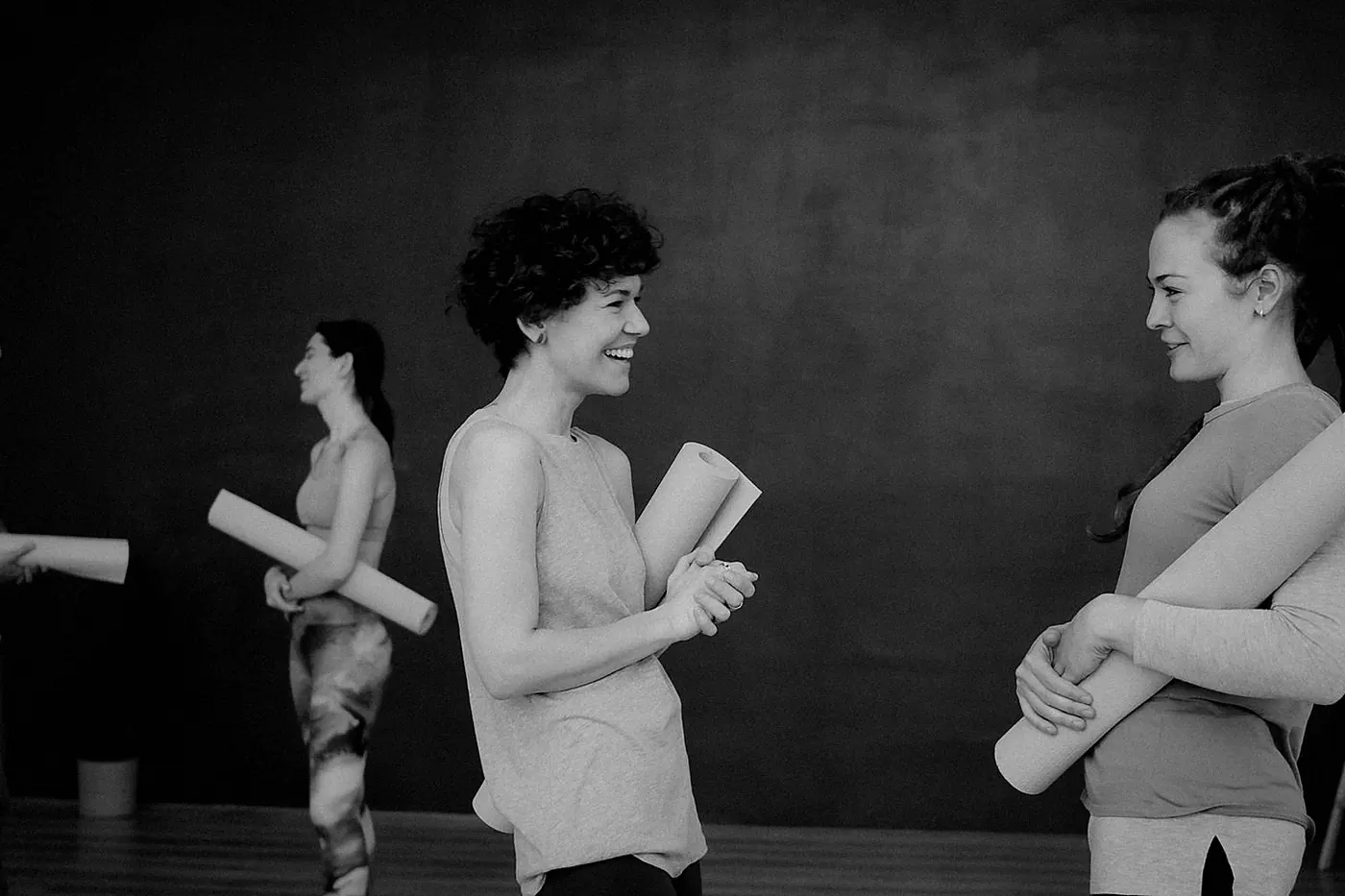Three people holding rolled mats and talking before a class