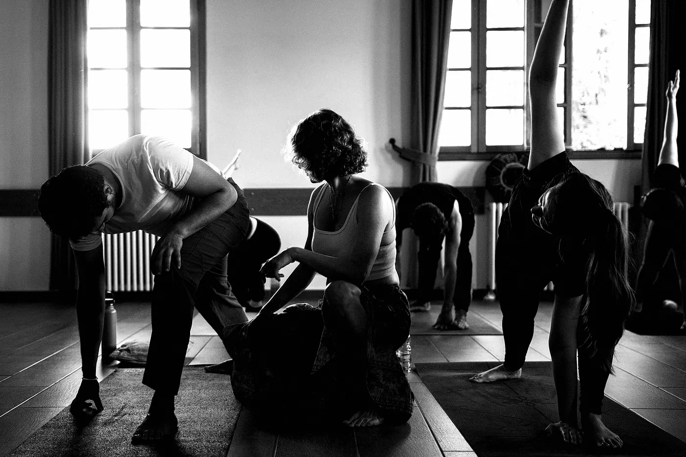 A teacher kneeling beside a student to adjust her forward bend