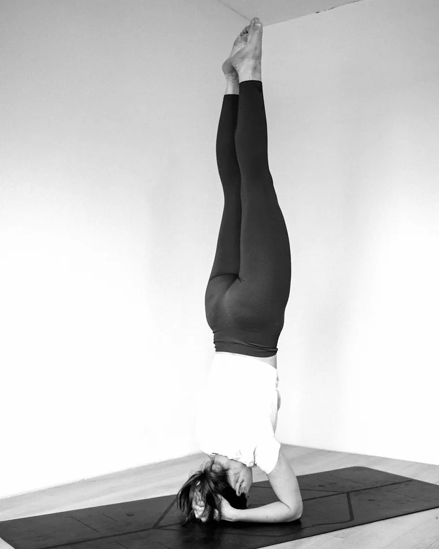 A woman holding a headstand on a mat in a white room