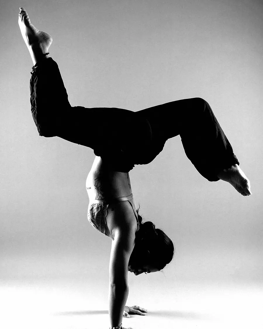 A woman in a handstand with her legs bent wide above her