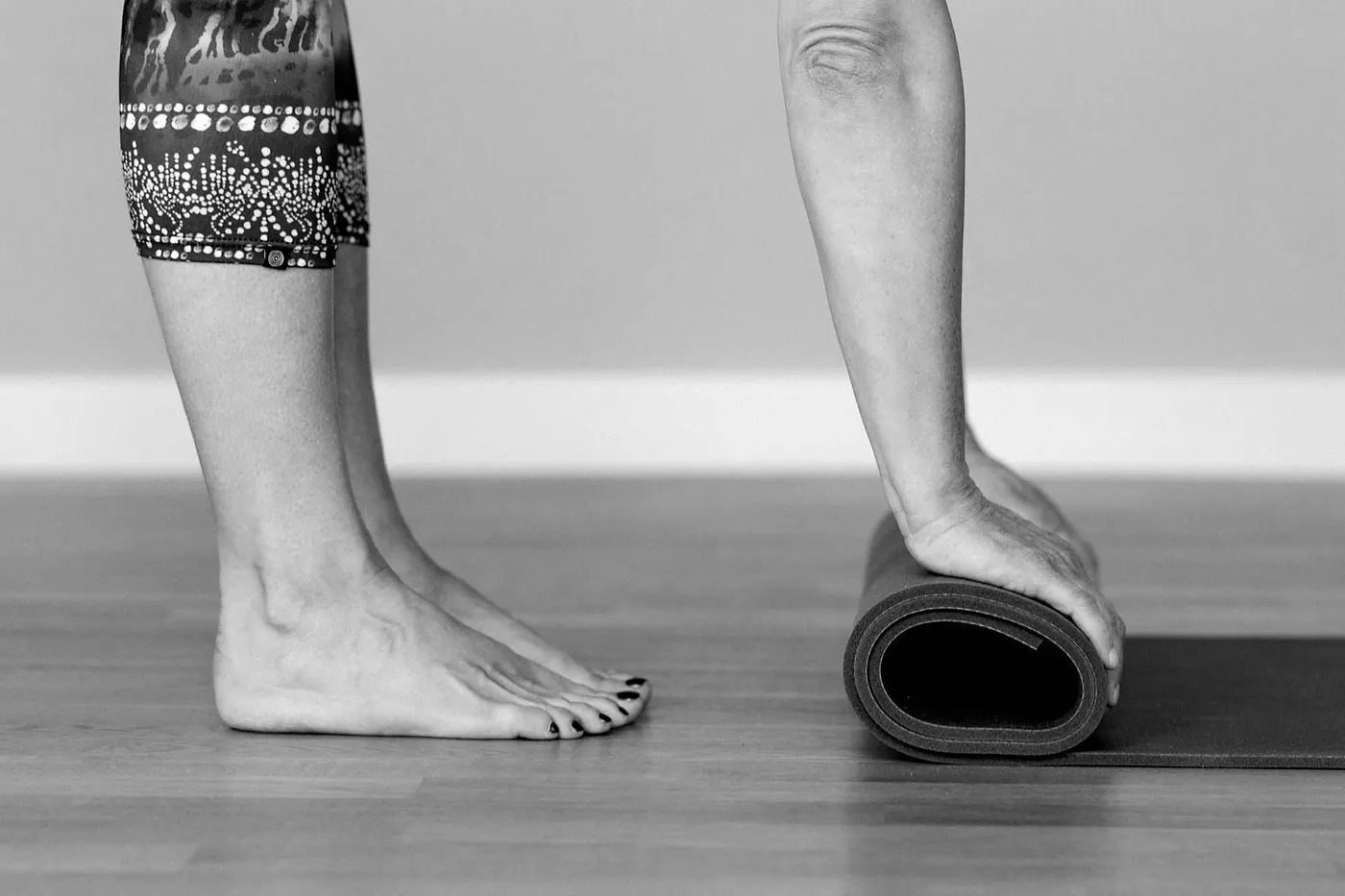 Bare feet next to a yoga mat being rolled up on a wooden floor