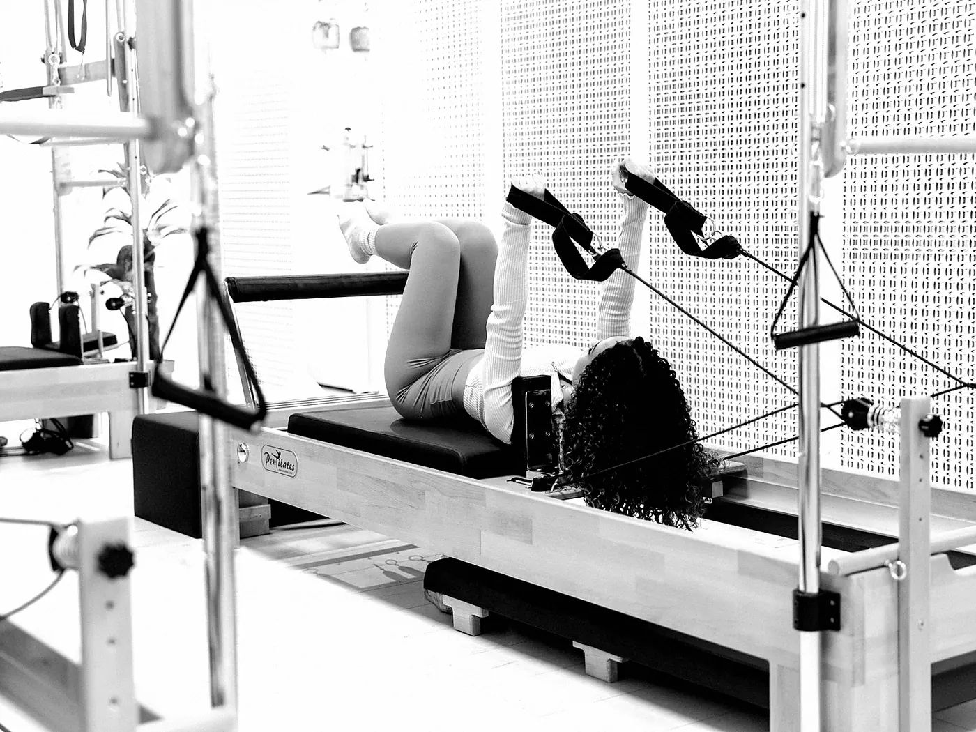 A woman on a reformer working with straps on her feet