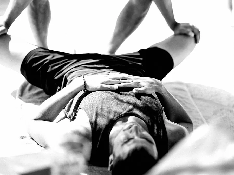 A teacher pressing gently on the hips of a student lying on a mat