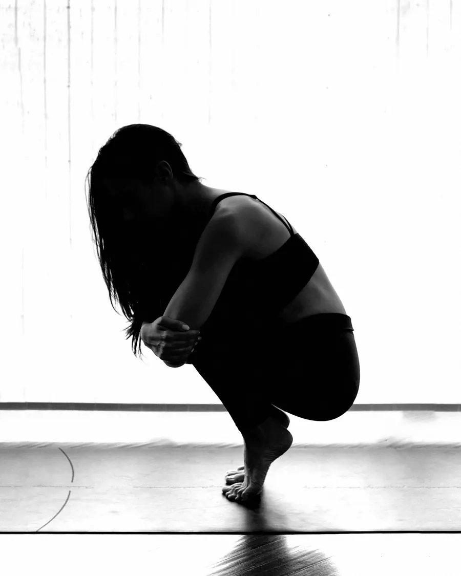 A woman crouching low with her arms around her knees, against a bright window