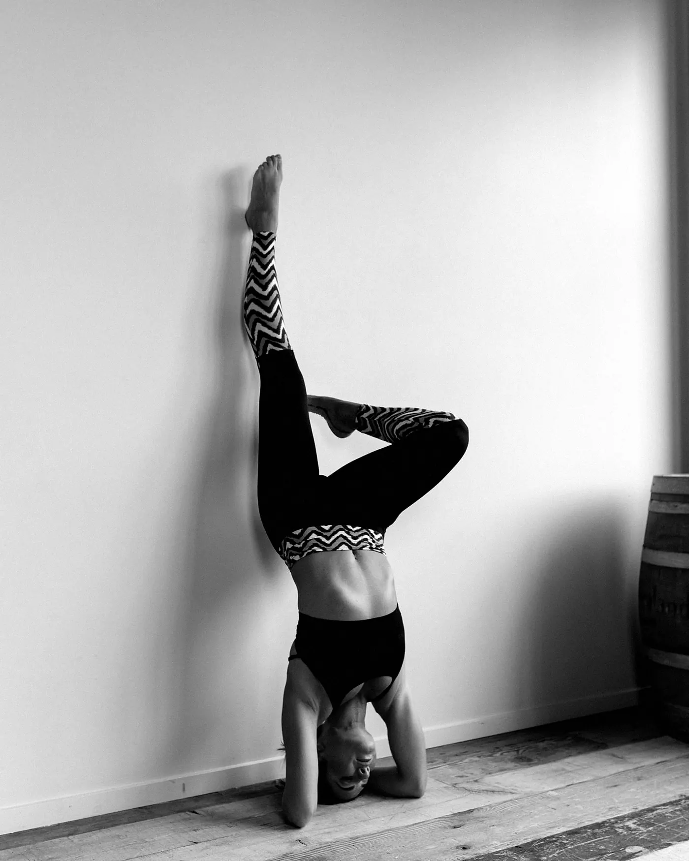 A woman in a headstand against a white wall with one knee bent