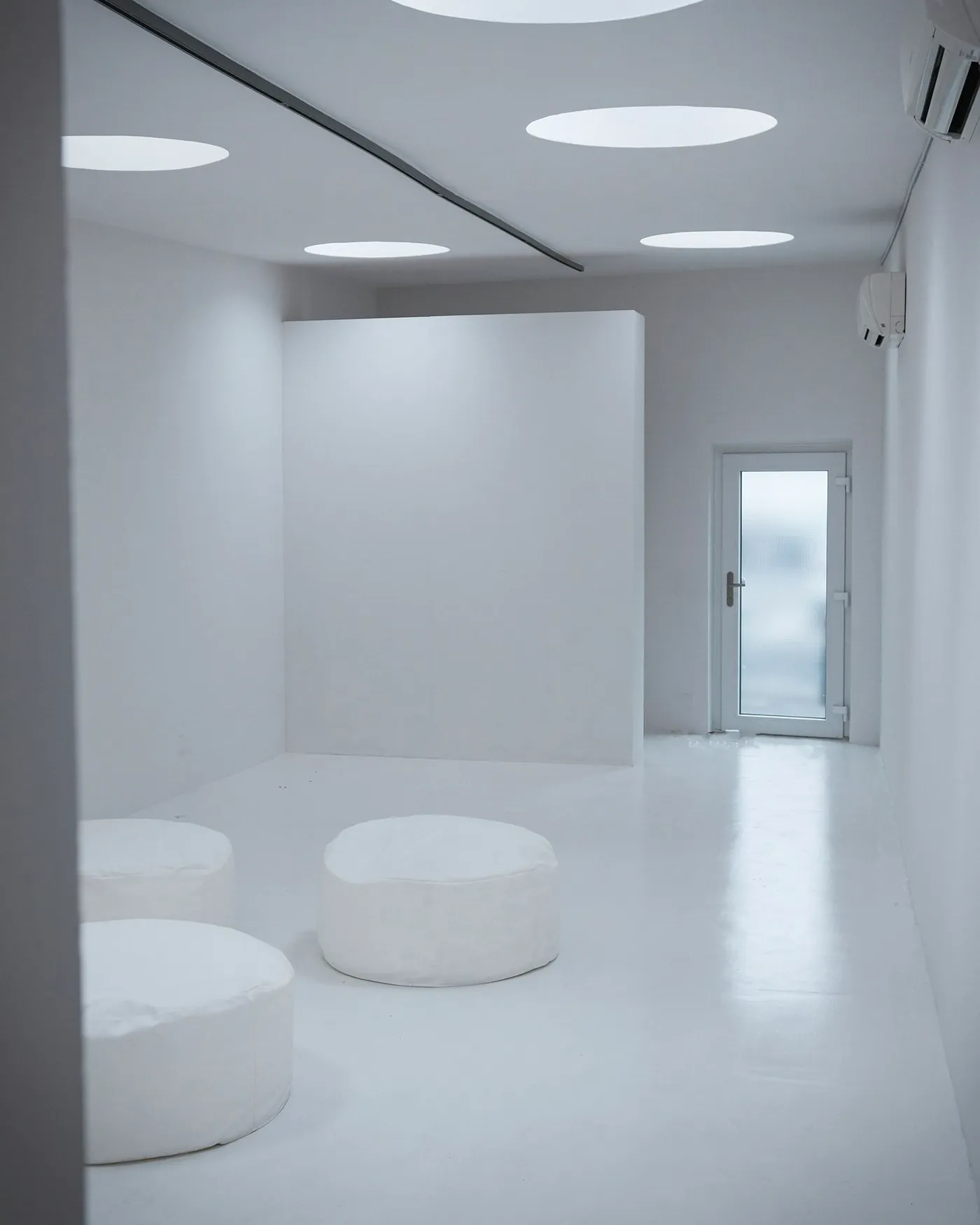 A white room with round white seats and a glass door at the back