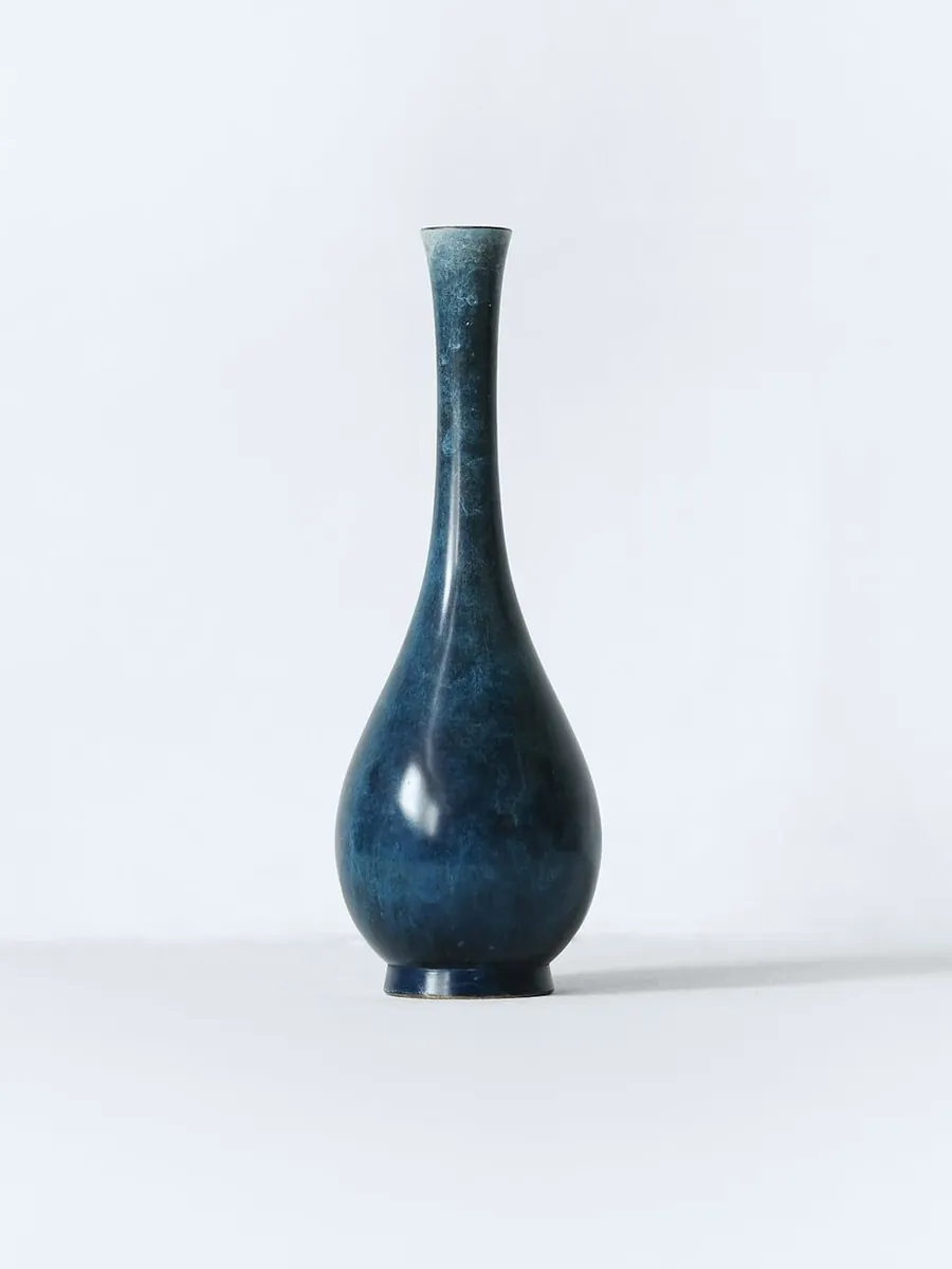 A slim dark blue porcelain bottle with a long neck, on a white surface