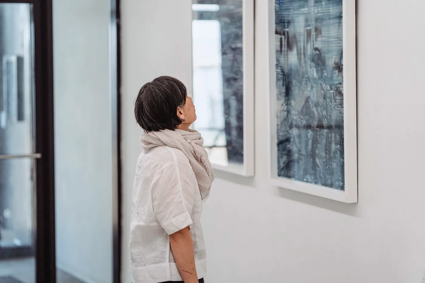 A visitor looking up at two blue abstract works in white frames
