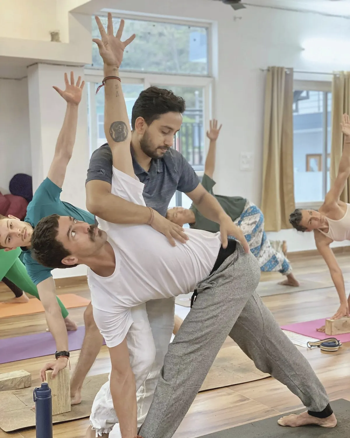 A teacher steadying a student in a wide standing pose during a class