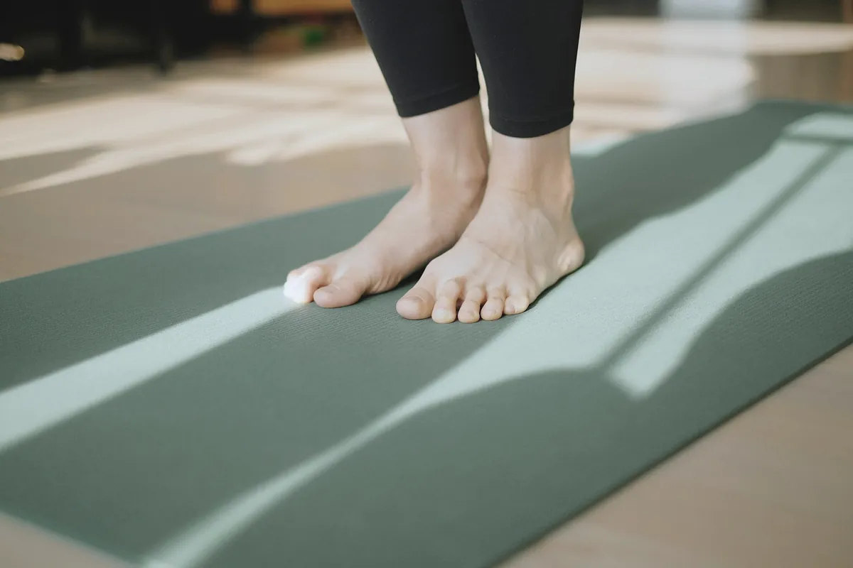 Bare feet standing on a green yoga mat in a stripe of sunlight
