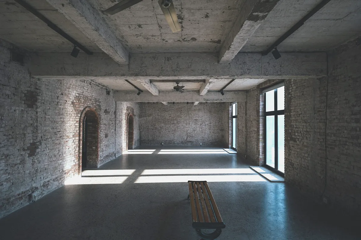 A long empty hall with brick walls, a wooden bench and sunlight from tall windows