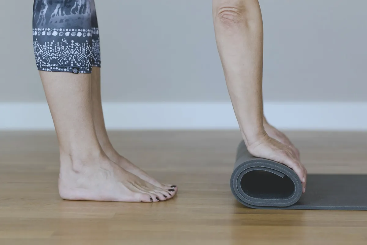 Bare feet next to a grey mat being rolled up on a wooden floor