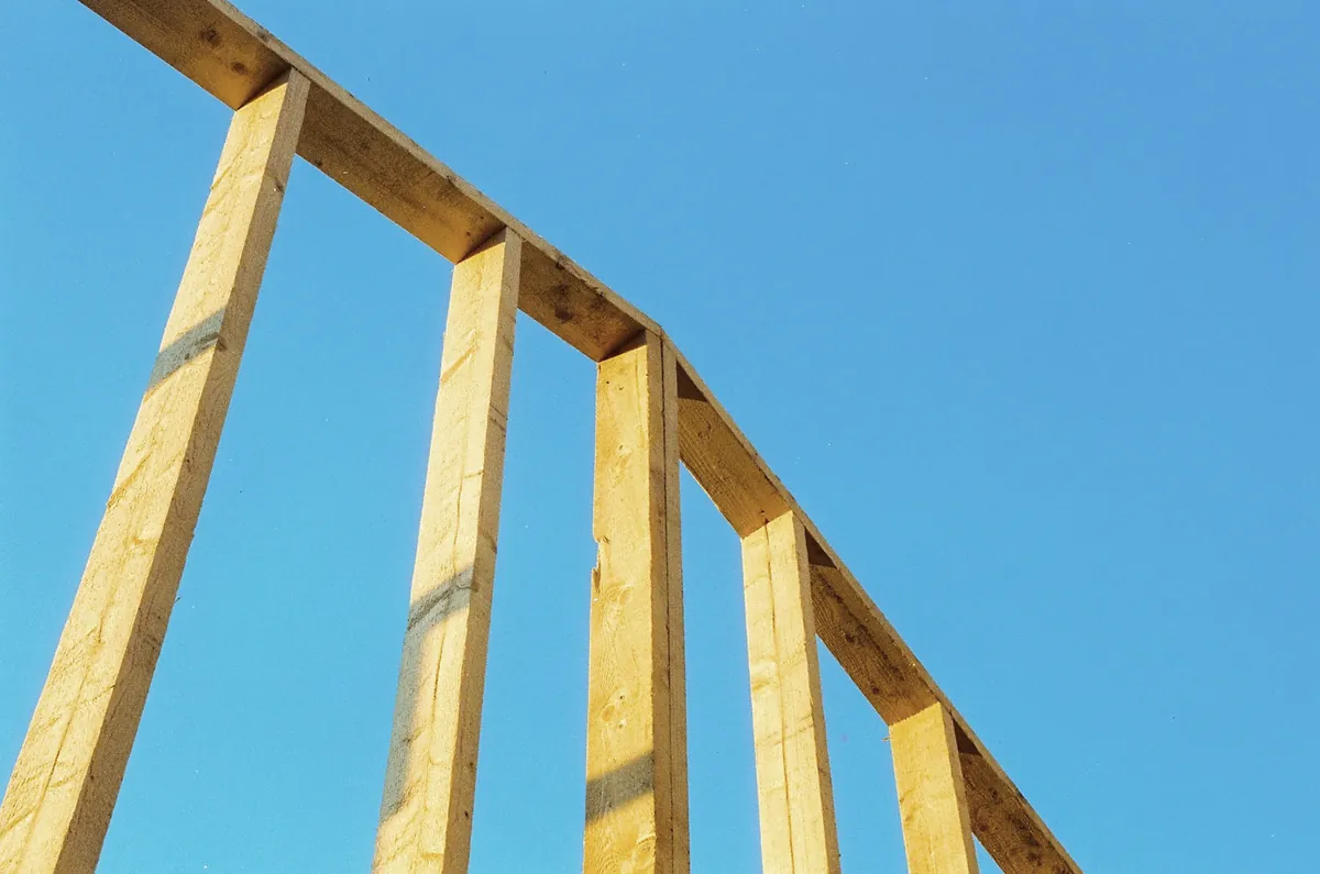Tall timber posts and a top beam of a new wall frame against a blue sky