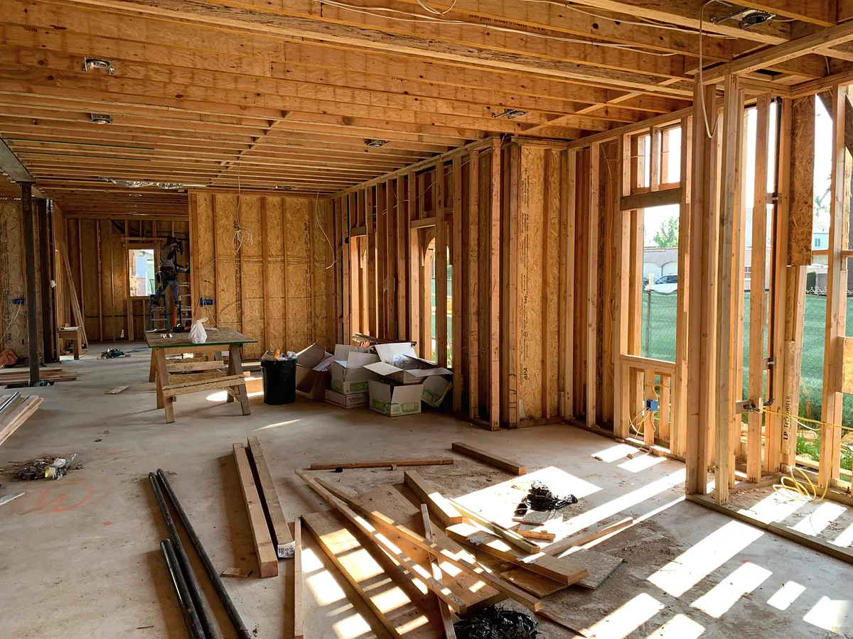 The timber wall frame of a new room with sunlight coming through the openings onto a plywood floor