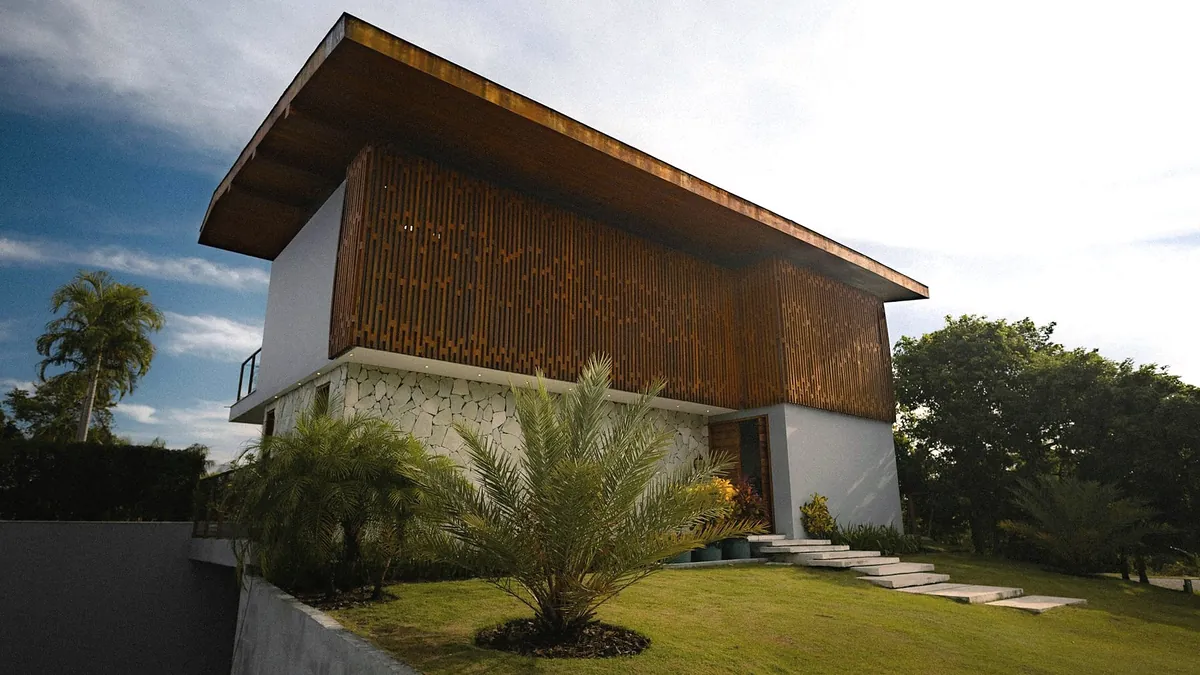 A house with a new timber upper floor behind vertical timber slats, a deep pitched roof, a white and stone ground floor and a garden with palms