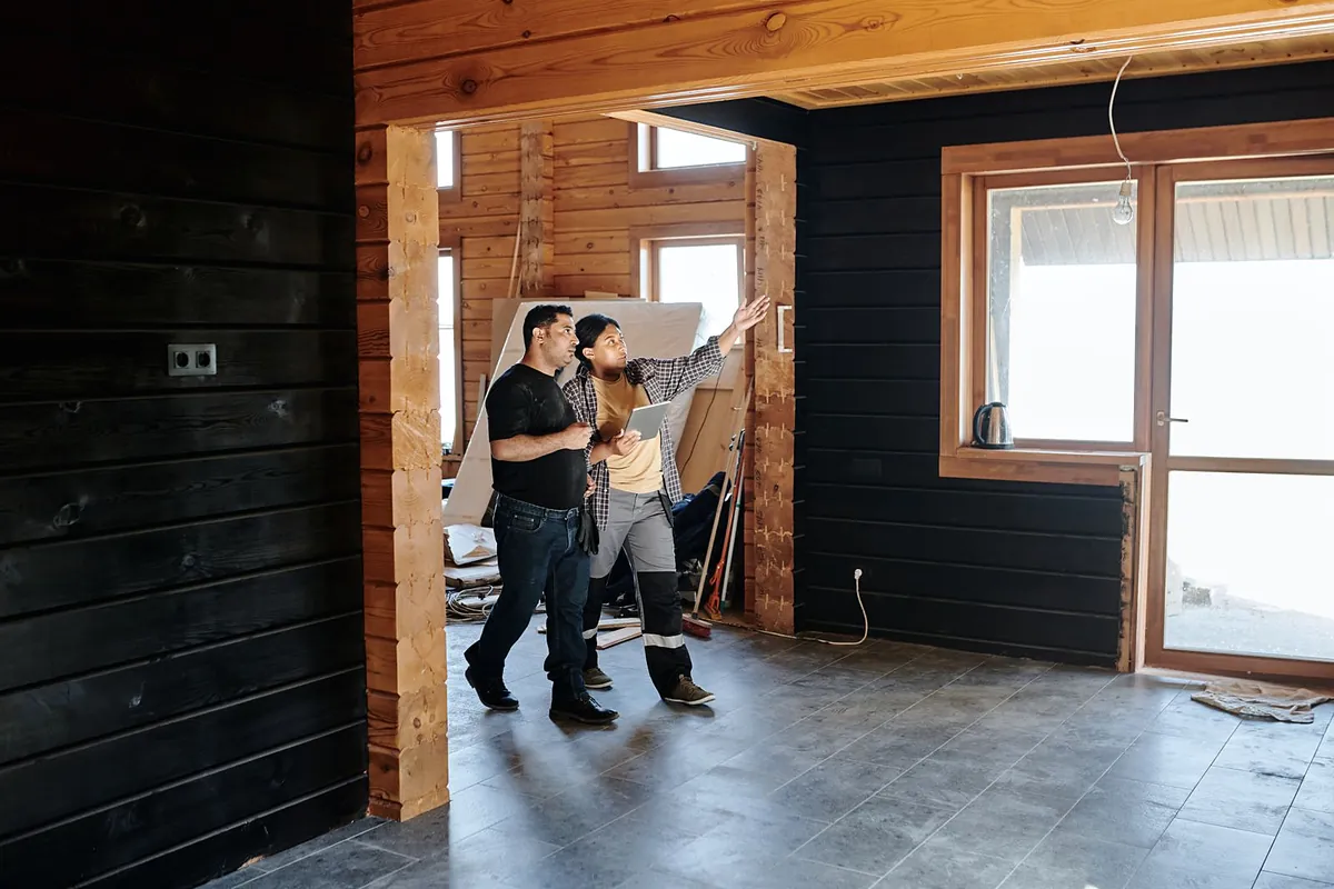 A site lead and an owner walking through a room with dark timber walls, pointing at the ceiling