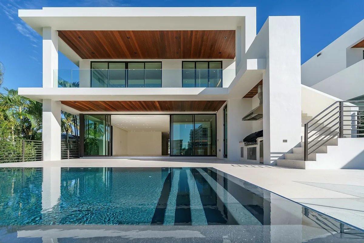 A white three-storey concrete house with timber-lined ceilings, large glass doors and a long pool with dark tile stripes