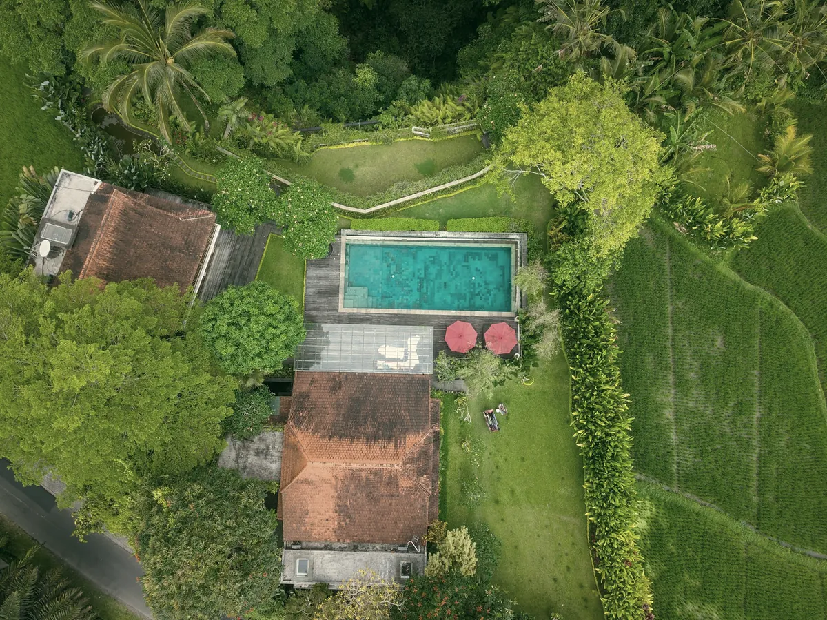 Aerial view of a house with an orange tiled roof, a pool and red umbrellas next to rice fields