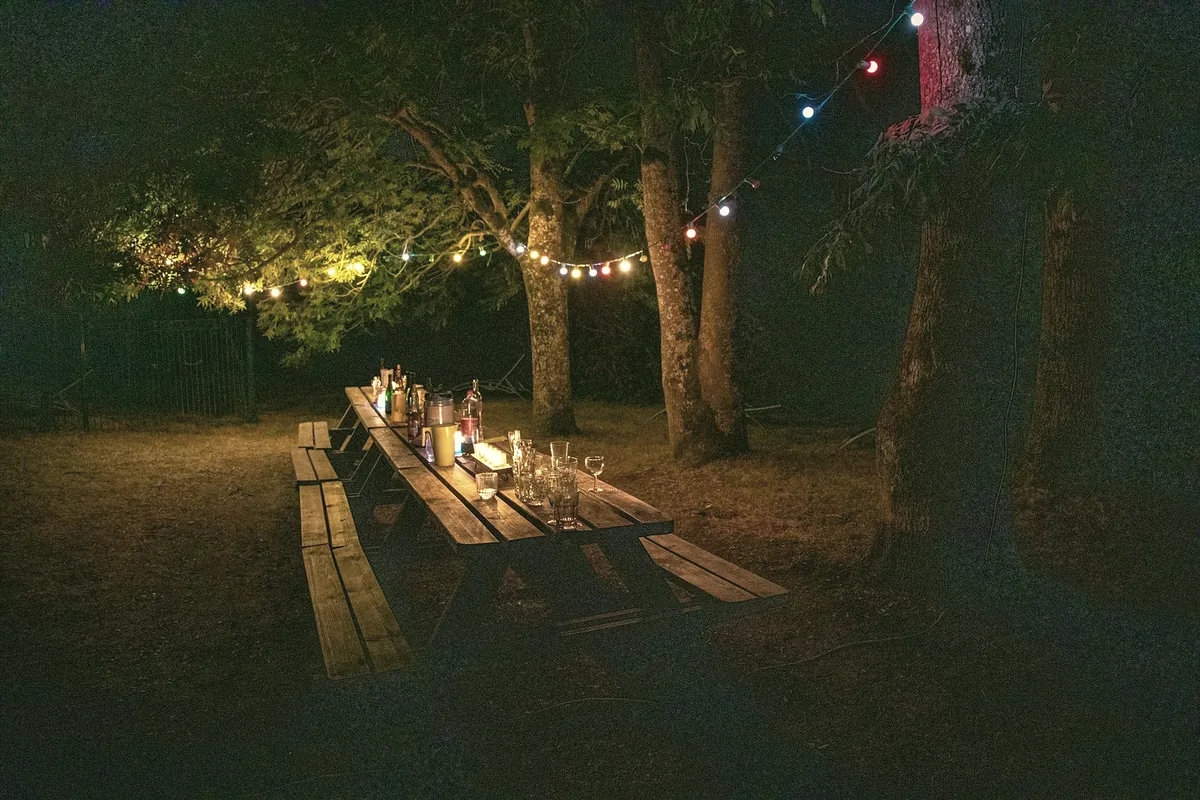 A long wooden table with candles under trees and strings of lights at night