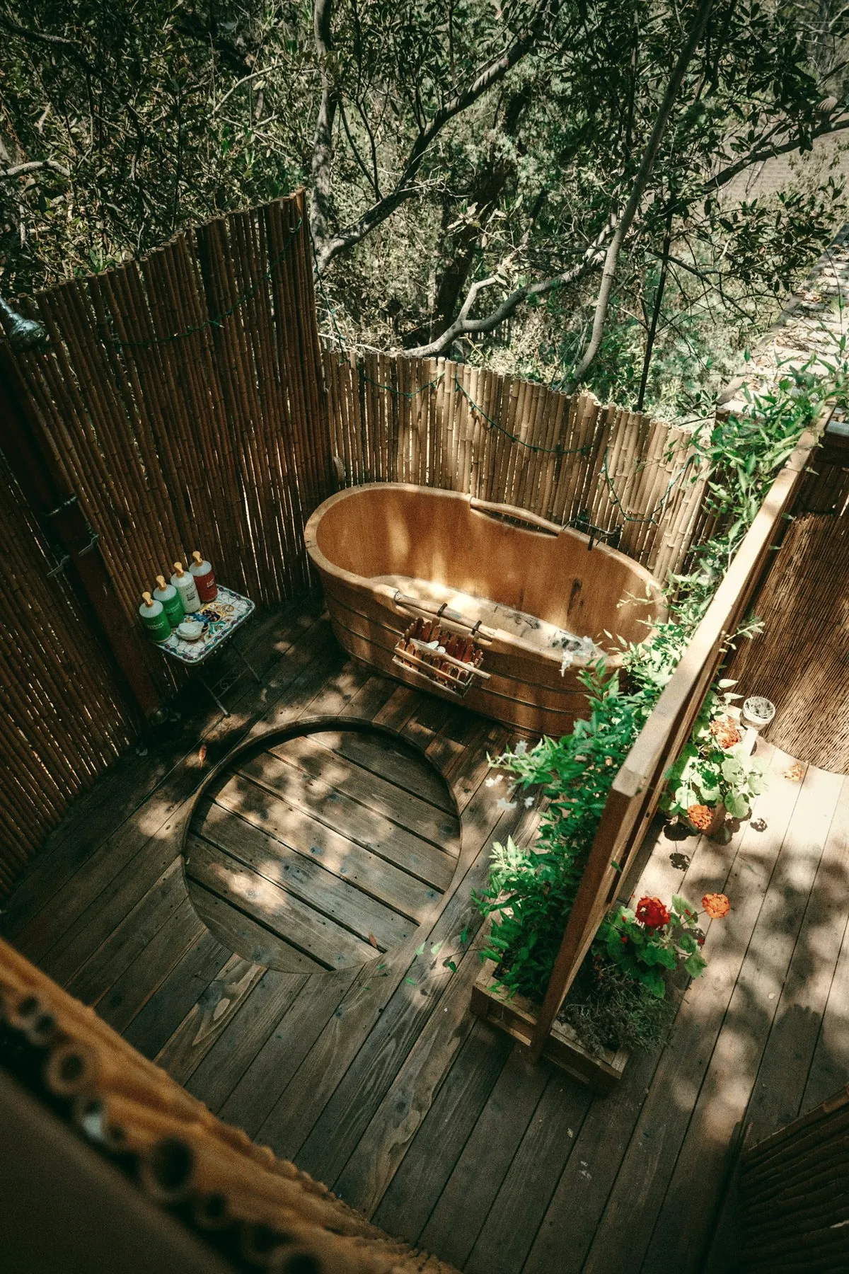 A copper bathtub on a wooden deck inside a bamboo fence, with plants along the edge