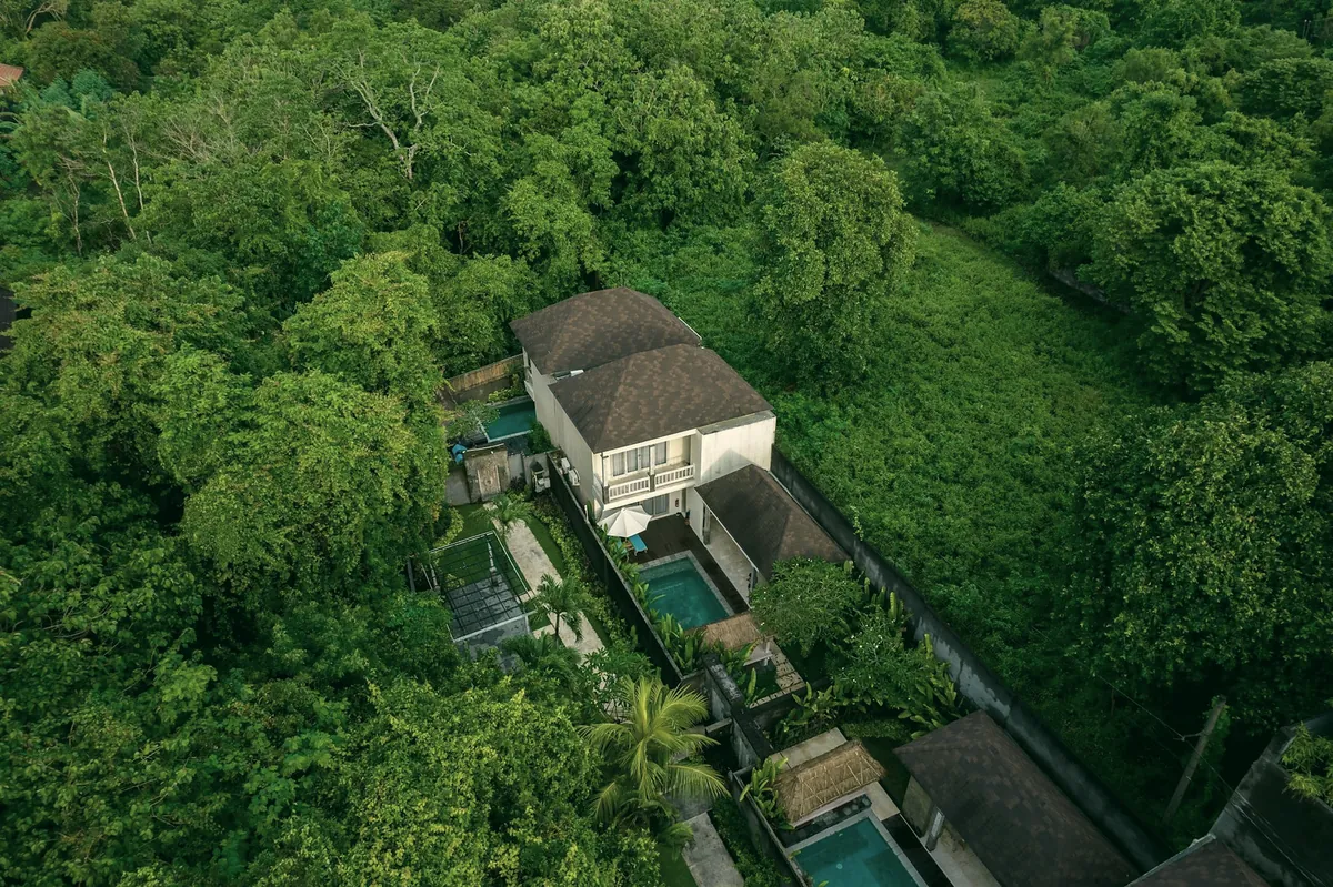 A two-storey house with a tiled roof and two pools, seen from above in thick green forest
