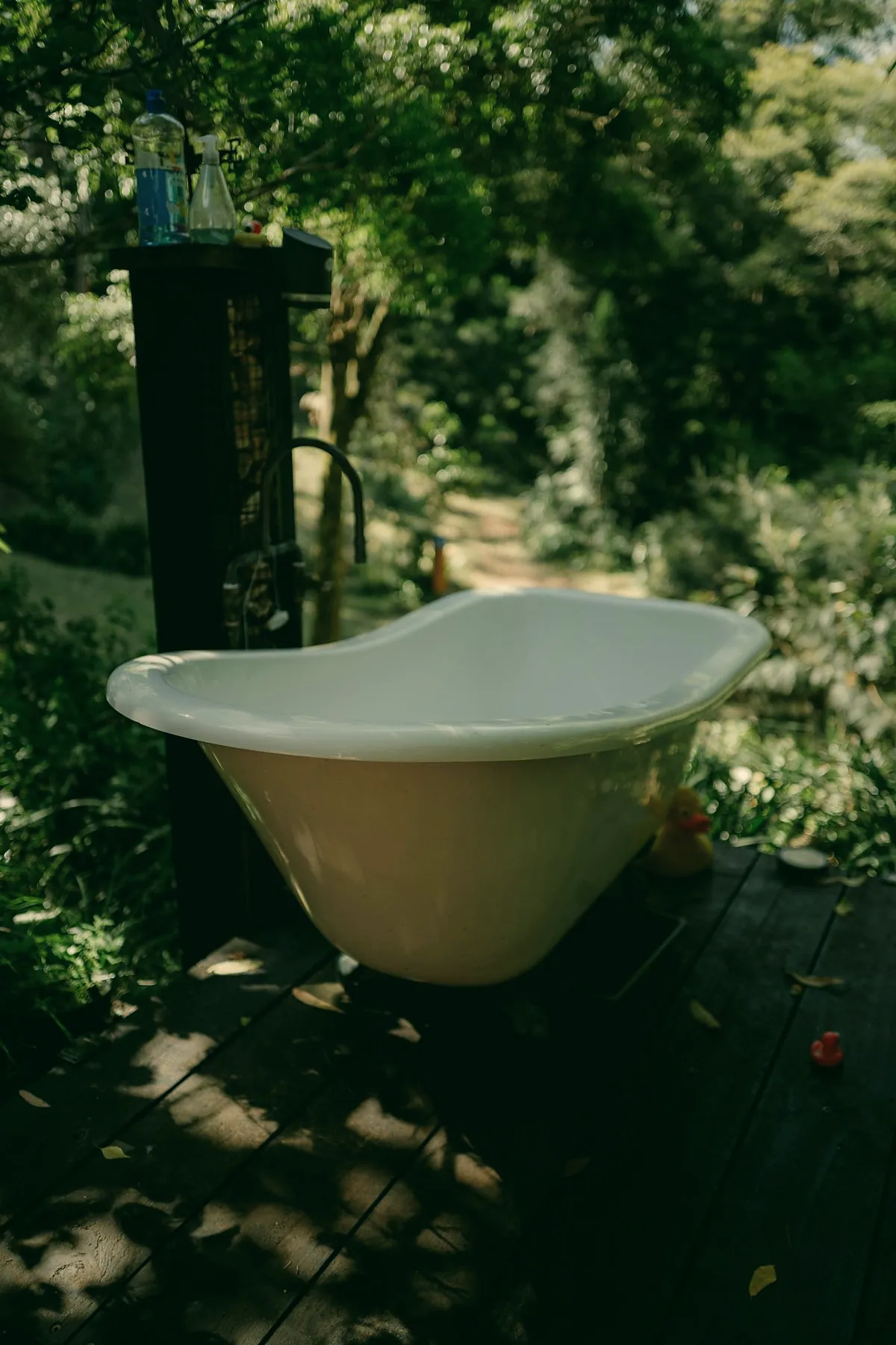 A white freestanding bathtub on a dark terrace in dense green garden
