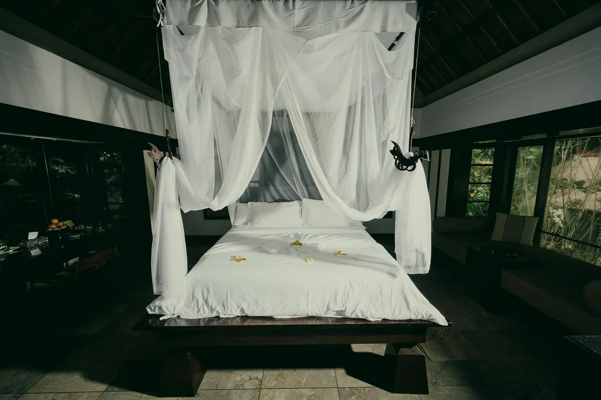 A canopy bed with white nets in a dark open-sided pavilion with a wooden roof