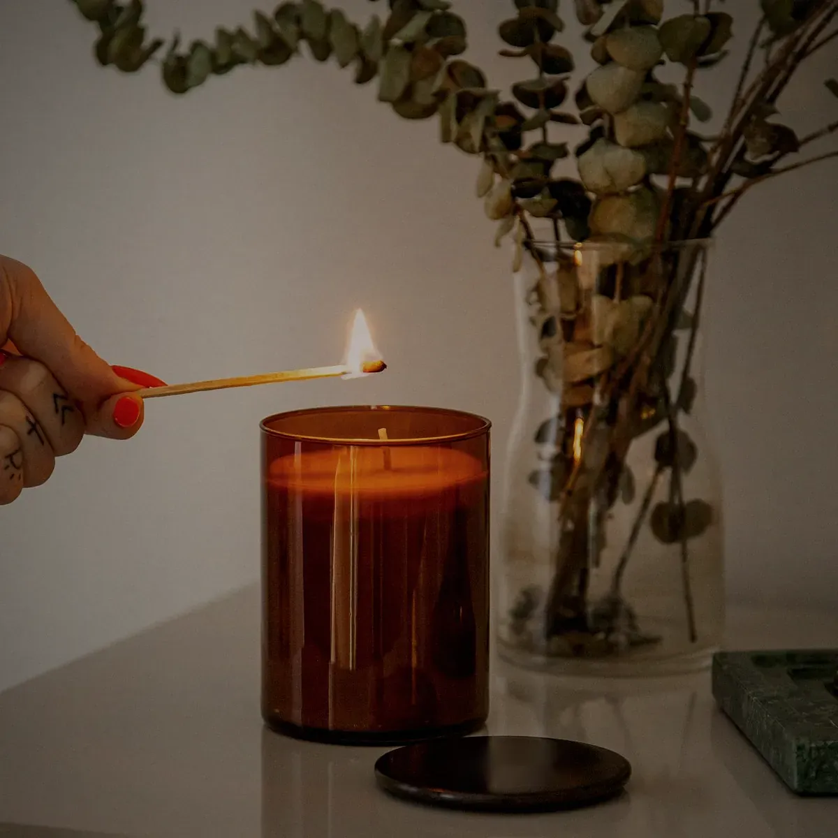 A hand lighting an amber jar candle with a long match