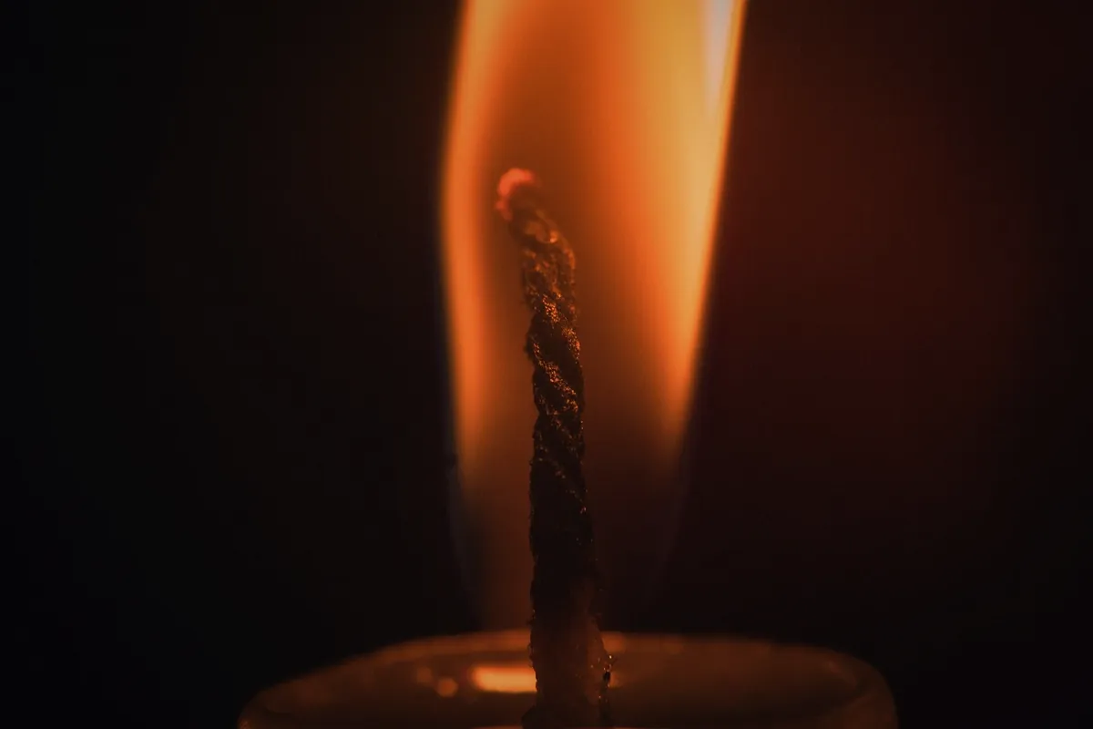 A close view of a candle flame and its wick, glowing amber