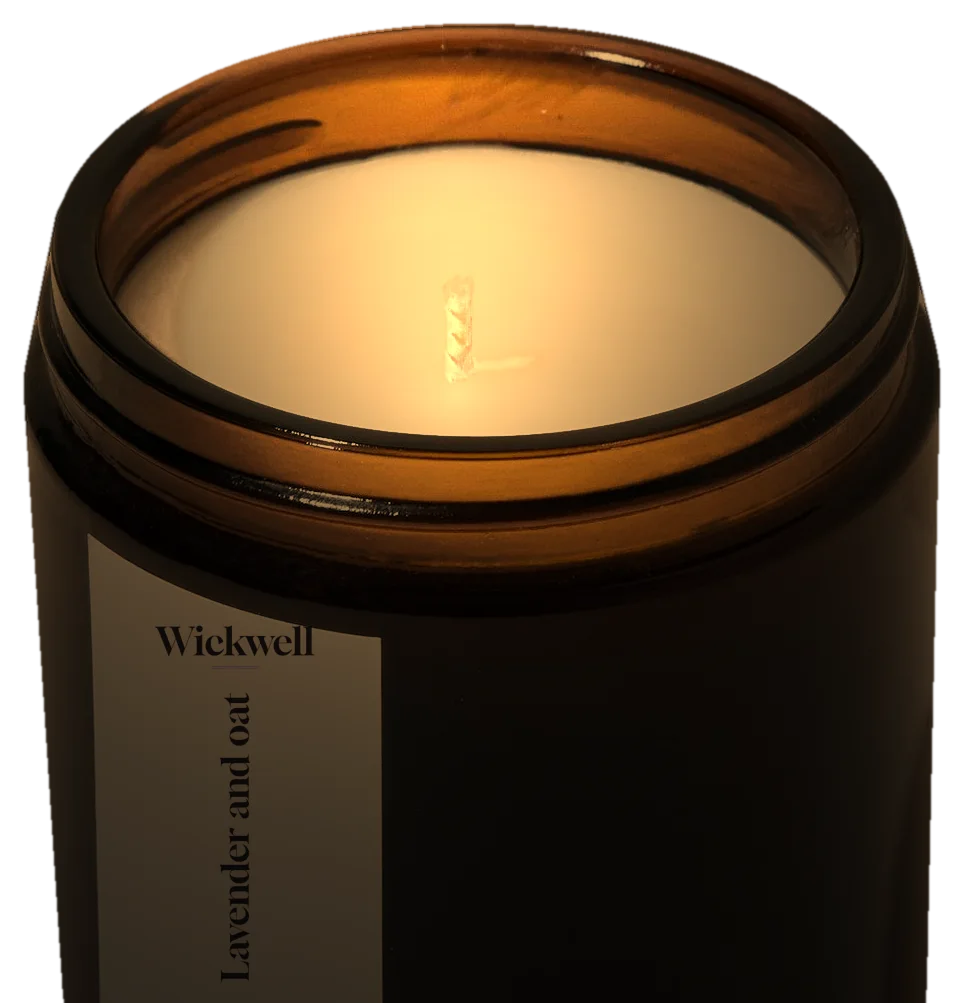 A lit candle in an amber glass jar with a Wickwell label that reads Lavender and oat