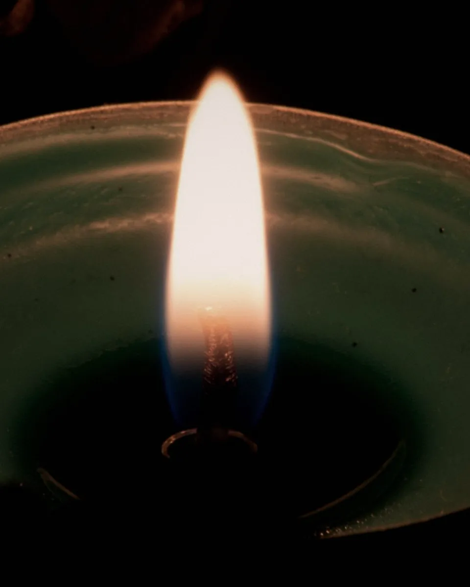 A candle flame burning in a pale green wax dish in the dark