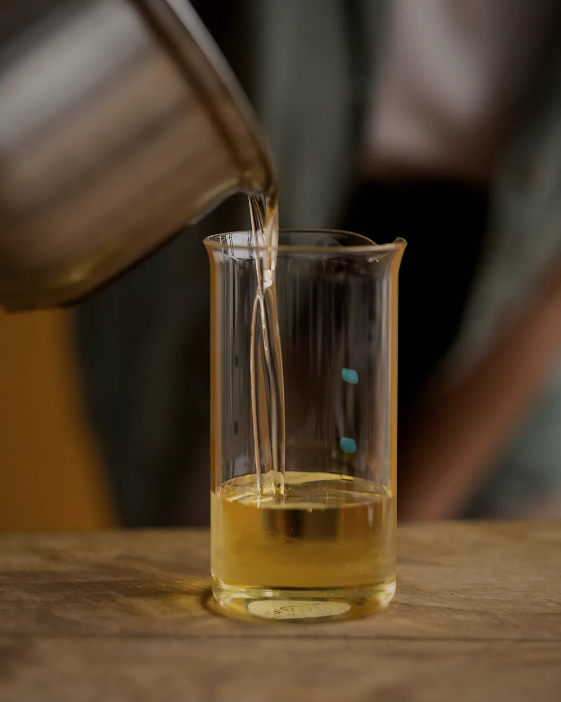 Melted wax being poured from a steel jug into a glass beaker