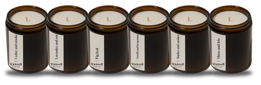 Six small Wickwell candles in a row on a shelf, one of each scent
