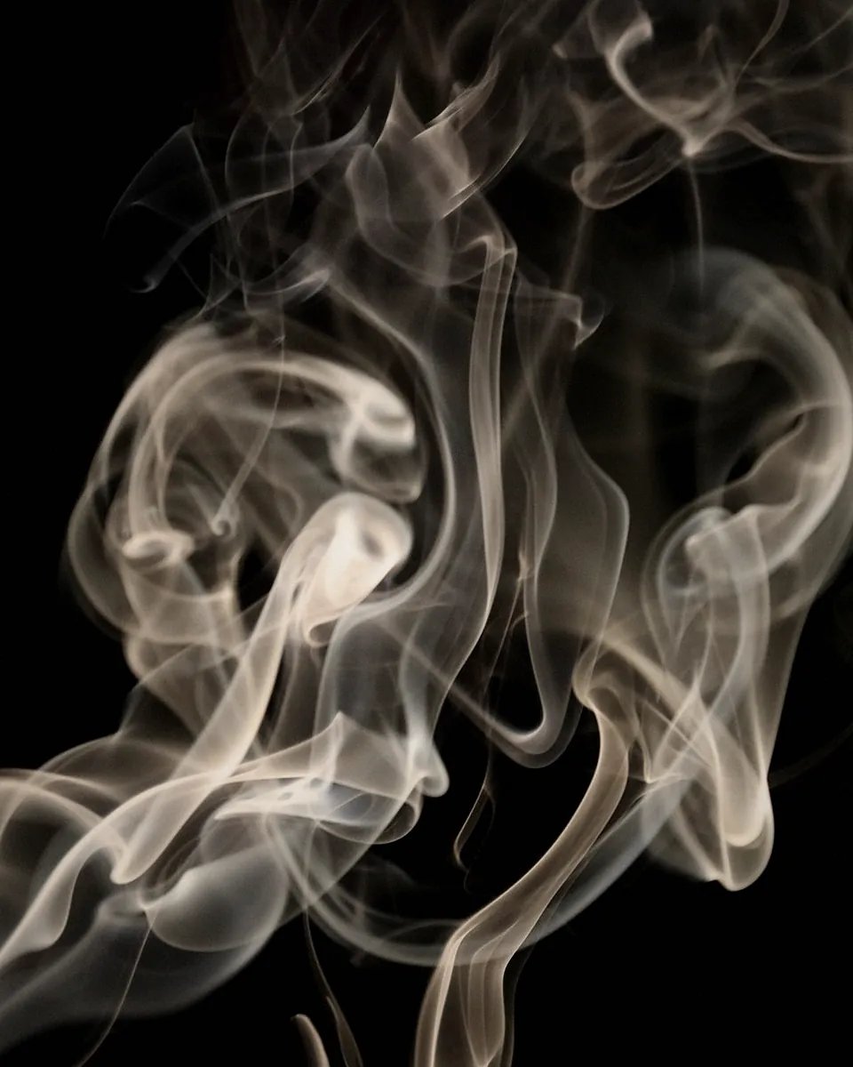 Smoke curling up from a blown out wick against a black background